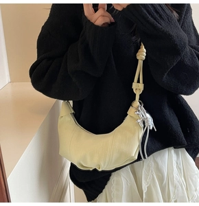 Detail view of a pale yellow crescent bag with textured material and silver charm accent