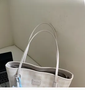 Close-up of beige plaid tote bag showing metal logo plate and durable double handles