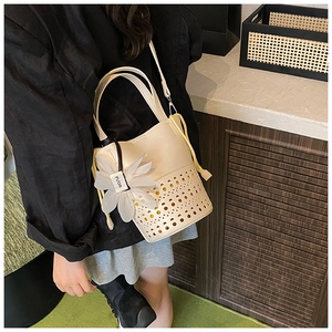 Détail du motif ajouré au laser et du charme floral sur un sac seau blanc crème