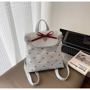 Detail of light gray backpack featuring red bow prints and a metallic heart pendant