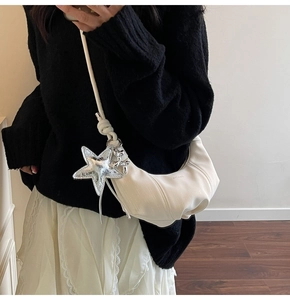 Detail view of a cream crescent crossbody bag with silver star and dog metal charms