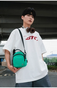Détail du sac bandoulière en nylon vert avec zips porté par un mannequin de style urbain