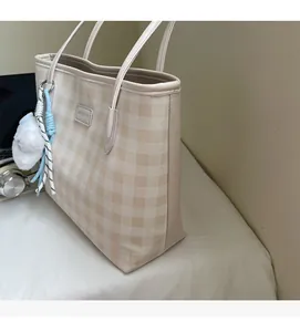 Detail of beige checkered tote bag with plush ball charm and logo label showing canvas texture