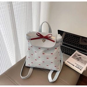 Detail of light blue bow backpack with heart pendant on a leather stool near a laptop