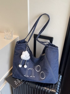 Deep blue denim tote bag with h°o embroidery and white plush cloud charm on a suitcase