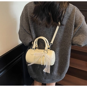 Détail d'un sac seau beige cylindrique avec un nœud en dentelle et une chaîne de perles