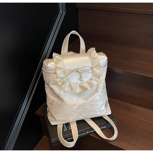 Detail of cream bucket bag with decorative bow, ruffled flap and pearl charm on a book