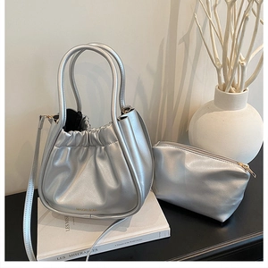 Silver pleated bucket bag and matching zipper pouch set shown on decorative books
