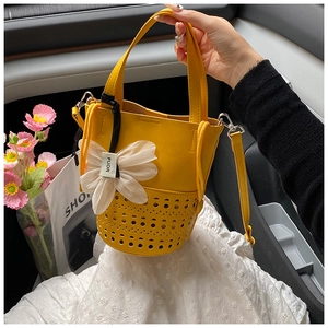 Détail du sac seau en cuir jaune avec motifs ajourés au laser et breloque fleurie