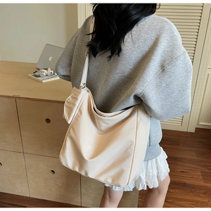 Close-up of beige nylon tote bag with wide strap and side pouch on model in casual setting