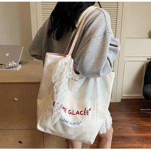 Detail of off-white canvas tote bag featuring French embroidery and a lace scarf accessory