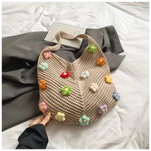 Détail d'un sac cabas beige crocheté à la main avec fleurs colorées en 3D sur un lit