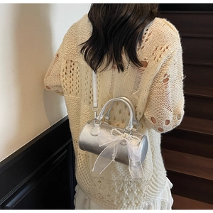 Sac cylindre argenté avec nœud en dentelle et perle porté à l'épaule par un mannequin