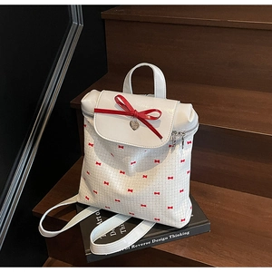 Detail of white backpack with red bow pattern and silver heart charm on black book
