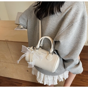 Détail du sac cylindre blanc avec nœud en dentelle, chaîne de perles et lettrage