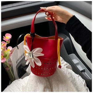 Détail d'un sac seau rouge ajouré en cuir avec cordon jaune et breloque fleurie élégante