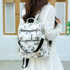 Detail of white leather backpack featuring black butterfly prints and a white fringe tassel