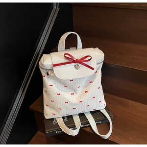 Close-up of white school backpack featuring red bows and a heart-shaped metal pendant