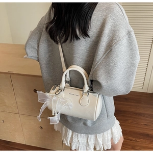 Détail du sac cylindre Boston crème avec poignées doubles et breloque ruban perle