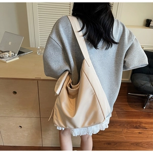 Minimalist beige slouchy hobo bag with wide shoulder strap worn by a model in a cozy room