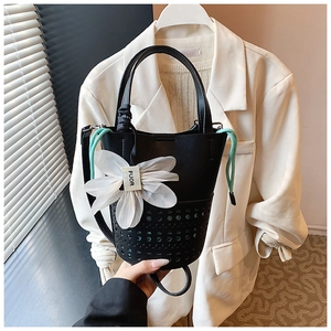 Détail du sac seau noir avec motifs ajourés au laser et pendentif fleur blanche