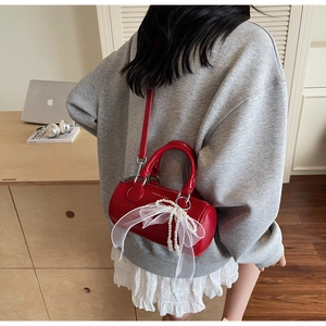 Détail du sac cylindre rouge avec breloques en perles et nœud en tulle pour femmes