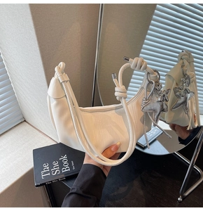 Detailed shot of white half-moon bag featuring a knotted strap and silver star pendant