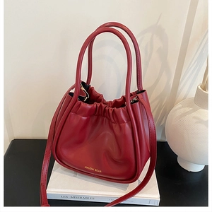 Detail of dark red pleated leather handbag with hard handles and golden brand logo