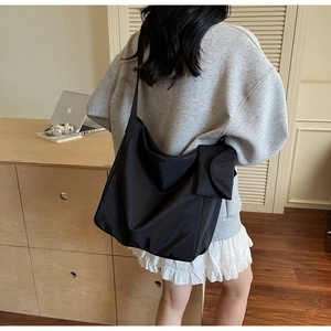 Close-up of black nylon crossbody bag featuring a functional side flap pocket on model