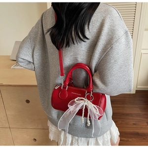 Détail du sac seau cylindrique rouge avec nœud en perles et texte de mode gravé