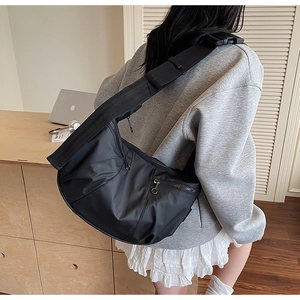 Model view of a large black nylon dumpling bag showing practical size and wide shoulder strap