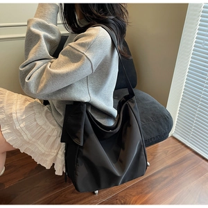 Side view of a large black nylon tote bag with a slouchy design on a model's shoulder