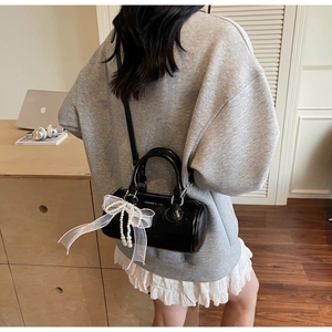 Détail du sac cylindrique noir brillant avec nœud en dentelle blanche et breloque en perles