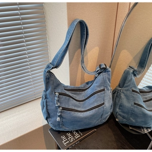 Detail of blue denim tote bag with three zippers and a wide strap in a home setting