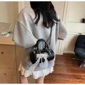 Détail d'un sac cylindrique noir avec nœud en dentelle et perles sur une bandoulière