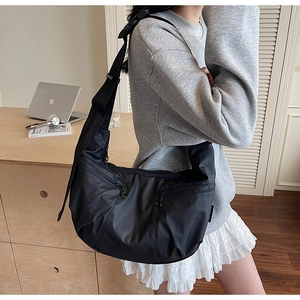 Close-up of a black nylon crescent crossbody bag with double zippers and wide strap