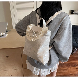 Detail of cream white backpack featuring ruffle edges, a bow knot, and pearl pendant