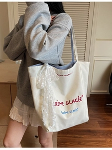 Large white canvas tote bag with red text and lace bow charm on model in a soft room