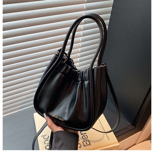 Detailed view of black pleated leather bucket bag with gold branding and top handles
