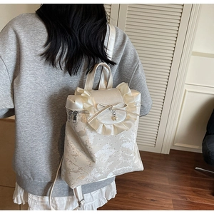 Rear view of model wearing a cream bow backpack with ruffles and pearl detail