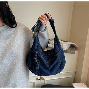Detail showing multi-zipper pockets and texture of dark blue denim crossbody bag