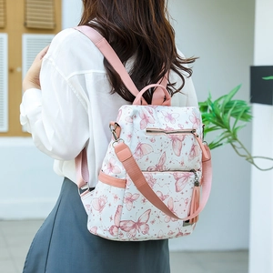 Detail shot of a white backpack with pink butterfly prints and decorative tassel charms