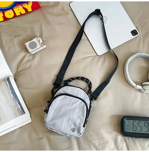 Sac bandoulière moderne en nylon gris avec tablette et casque sur un drap clair