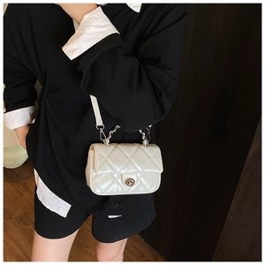 Detail of pearl white quilted mini crossbody bag with silver twist lock and metal chain strap
