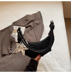 Detail of black hobo crescent bag with knotted handle and silver star pendant on white bedding