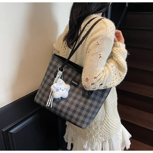 Checkered tote bag with plush cat charm shown on model in a retro interior setting