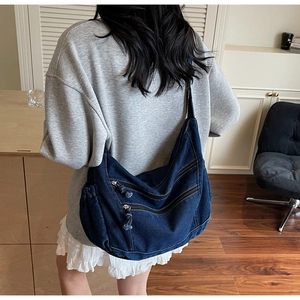 Detail view of denim crossbody bag with multiple zippers and wide comfortable shoulder strap