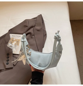 Detail of light blue crescent bag with rope strap and star charms against a suit