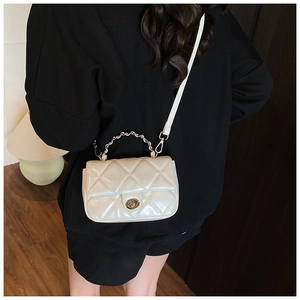 Detail of quilted leather crossbody bag in creamy white with metal chain strap and lock