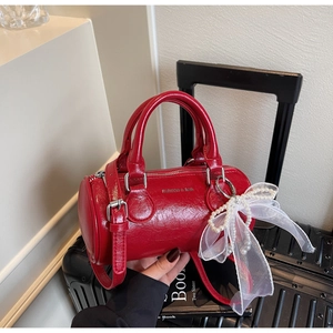 Détail d'un sac cylindre en cuir rouge avec pendentif nœud en perles et lettrage doré